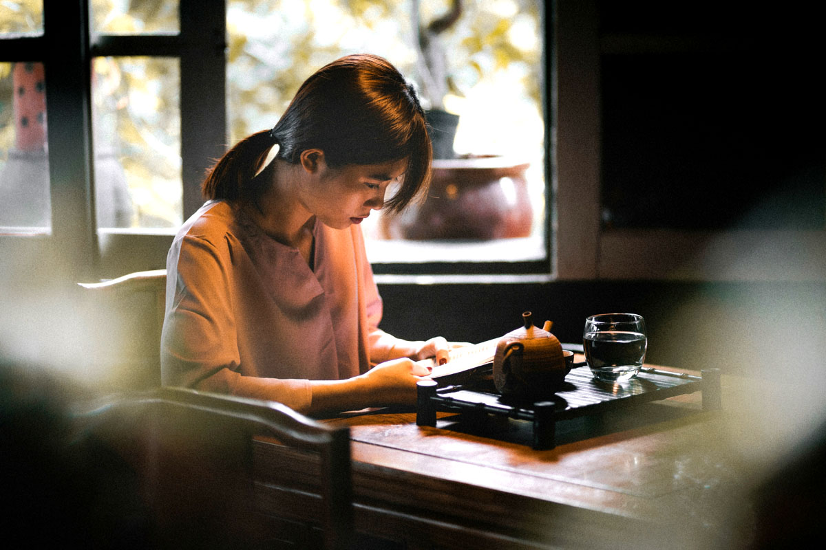A young woman sitting alone at a cozy cafe table reading a book for a slow living solo date.