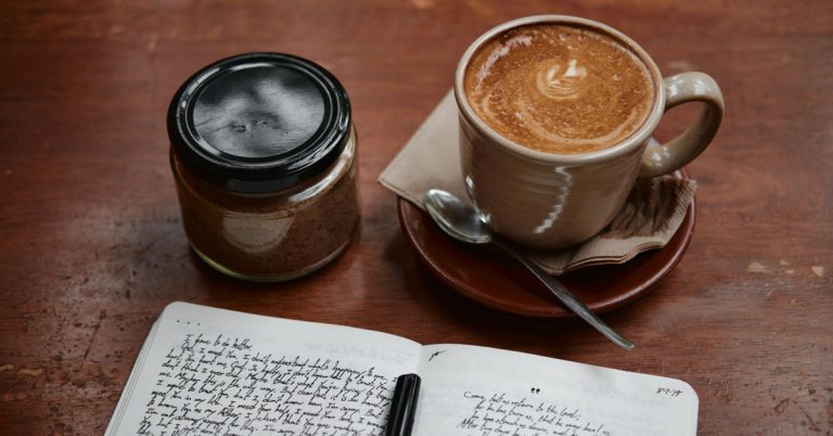 Cozy morning journaling setup with a cup of coffee and a glass jar on a wooden table for a January bucket list.