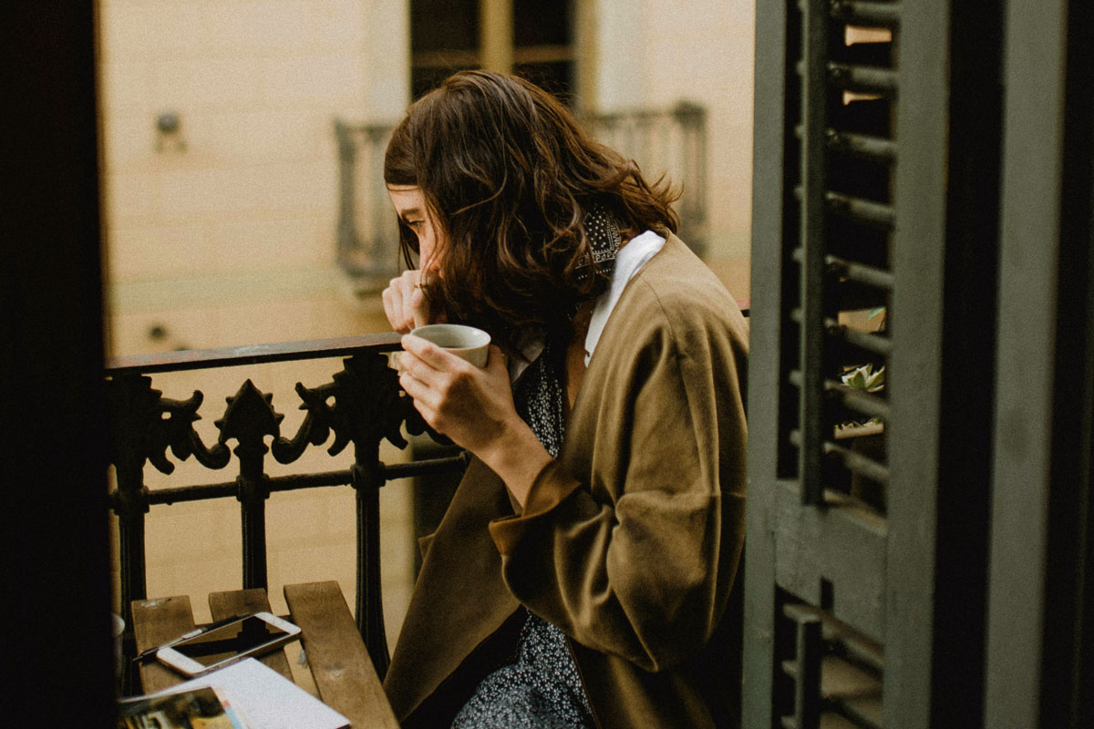 A woman sitting on her balcony writing in a paper journal to start a mindful and slow living winter routine.
