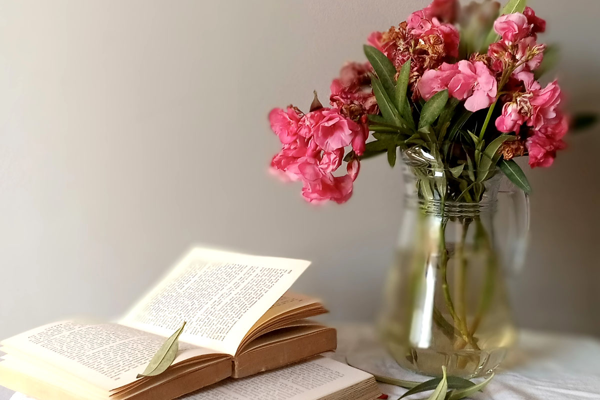 Open books arranged beside a glass vase filled with fresh, vibrant garden flowers, representing the mental health benefits of a slow-paced lifestyle.