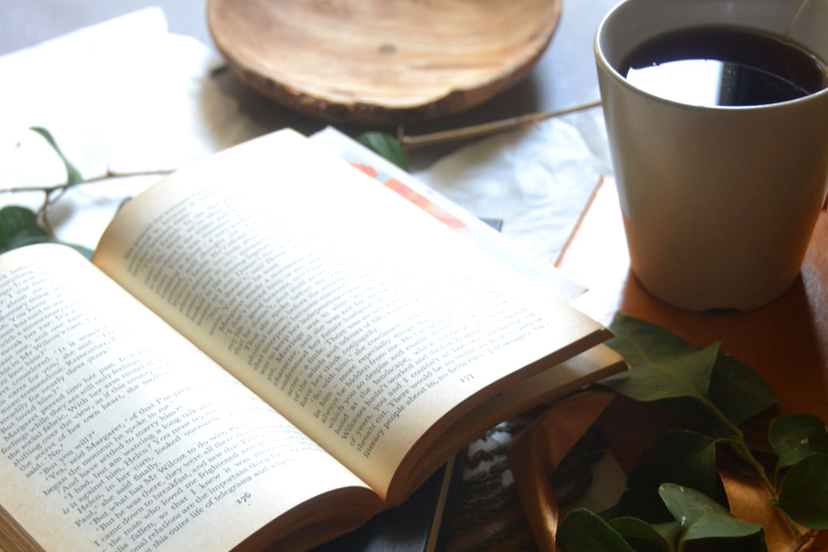 A minimalist and rustic tabletop setup with an open book next to an empty wooden bowl, symbolizing simple and quiet living habits.