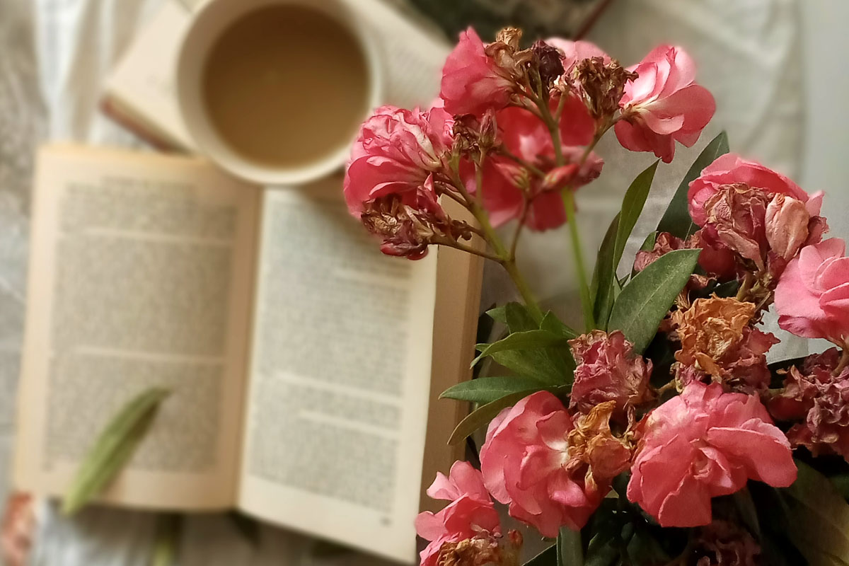 An open book on a table alongside a delicate bouquet of white flowers and a warm beverage, encouraging offline rest and editing your schedule.