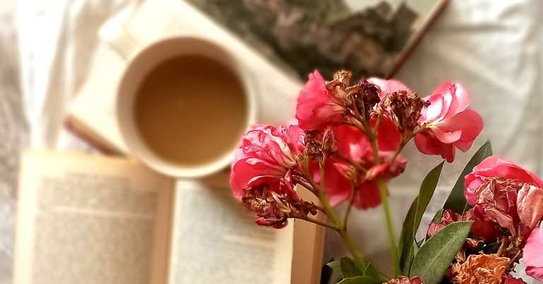 Two open paperback books resting on a light linen sheet next to a cozy cup of coffee, illustrating a slow living morning routine.