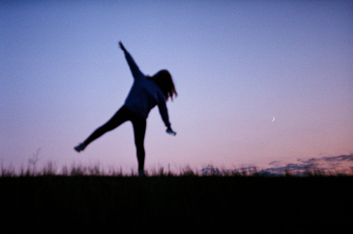 A silhouette of a woman dancing freely under a starry night sky and a bright full moon, celebrating emotional release.