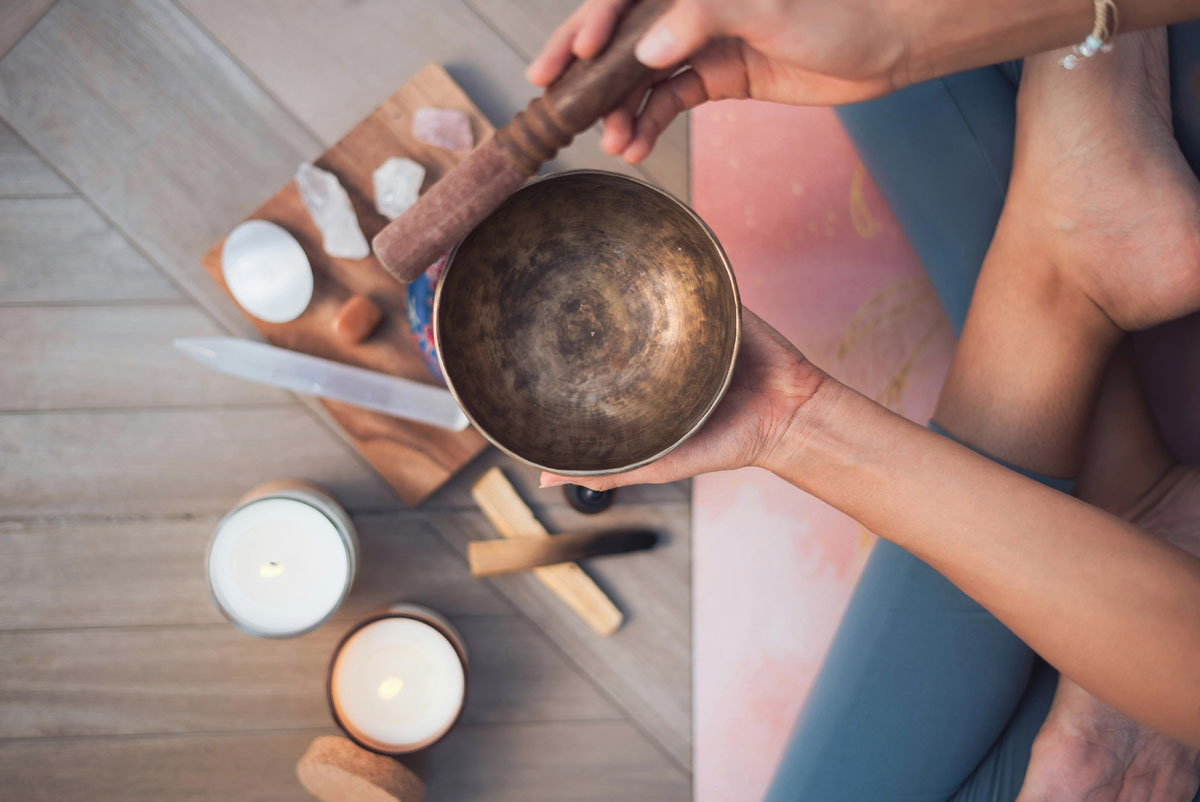 A brass Tibetan singing bowl next to crystals, illustrating an analog sound cleansing practice.