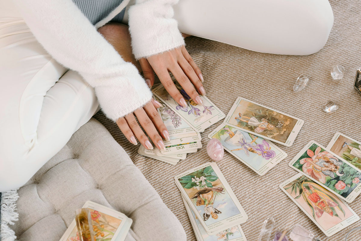 A woman pulling tarot cards from a beautifully designed deck laid out on a soft neutral fabric next to raw crystals.