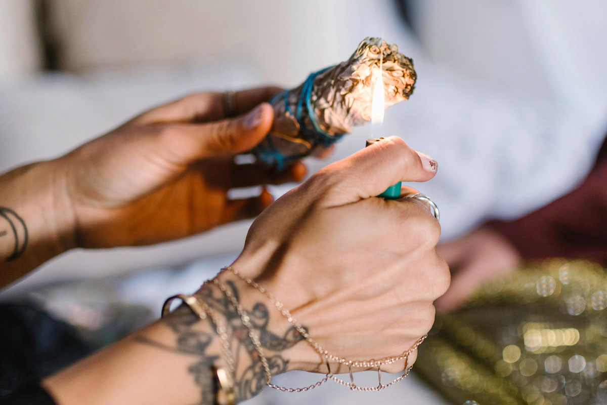 A woman with bracelets lights a bundle of herbs.