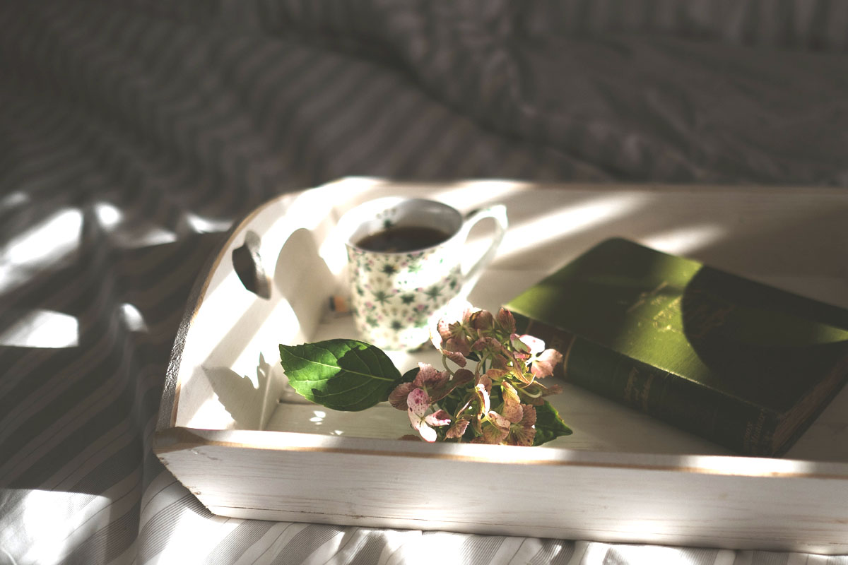 A mindfulness journal lays on a bed with flowers and a cup of coffee.