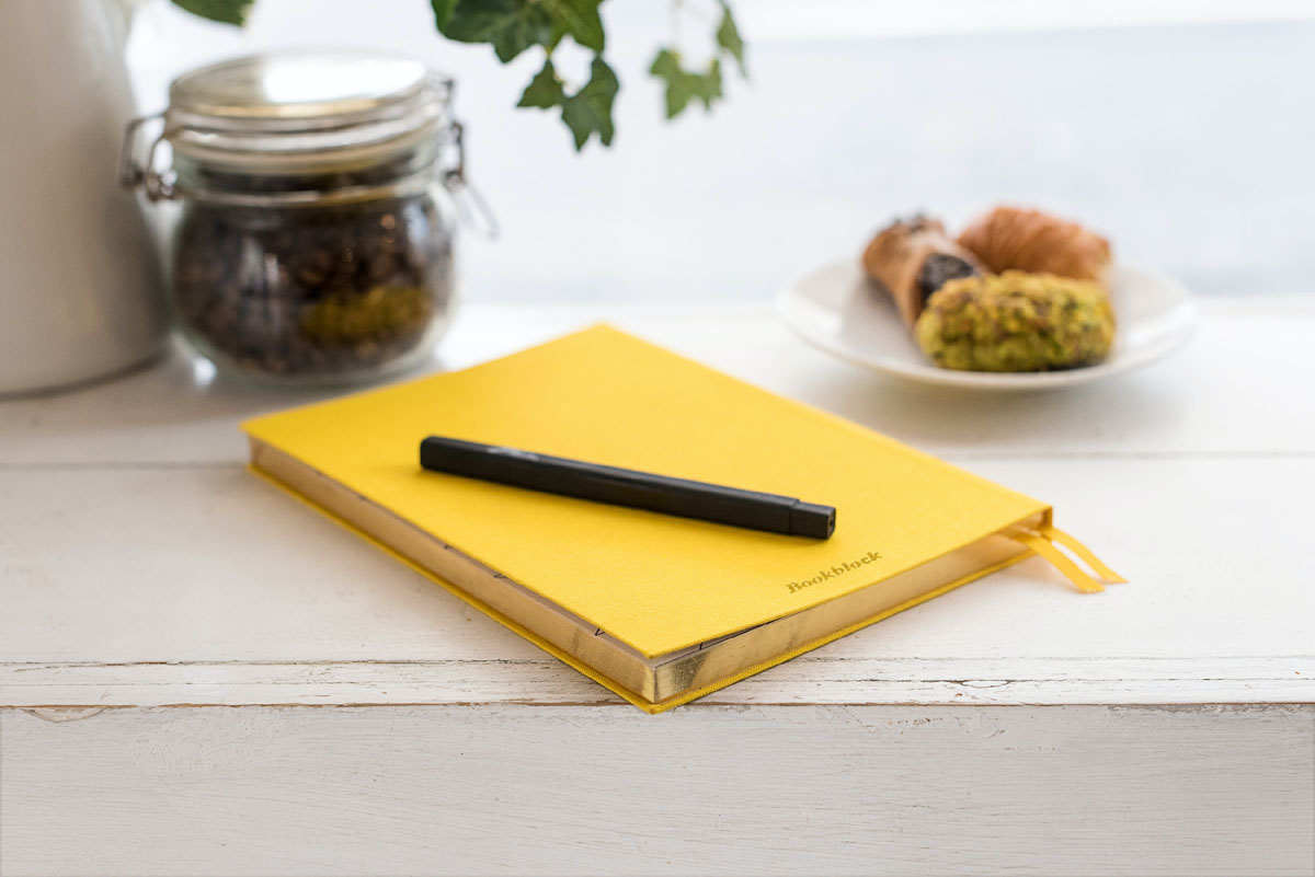 A yellow food journal lays on a table next to a plate of sweets.
