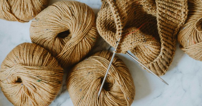 Cozy flat lay of warm beige yarn balls on a white table, representing creative hobbies and knitting.