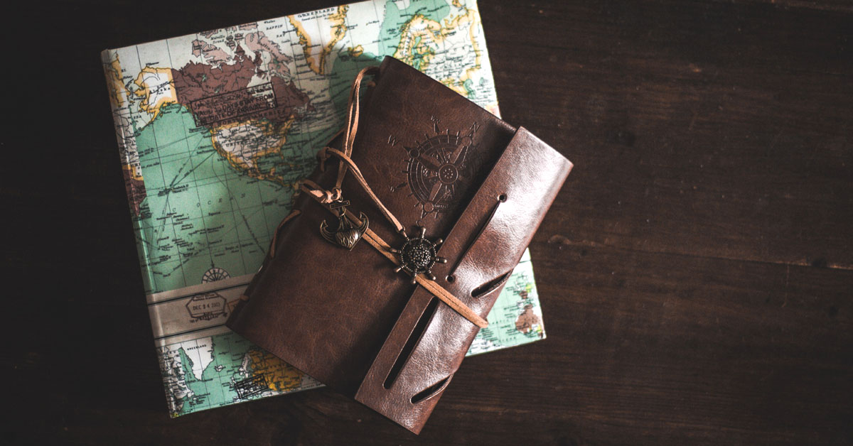 A travel journal lays on a desk on top of a map.