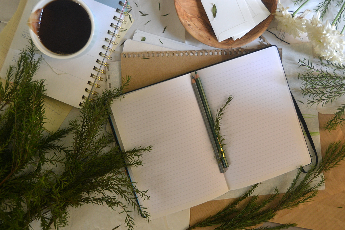 An affirmation journal lays open on a table next to leaves, tea and greenery.