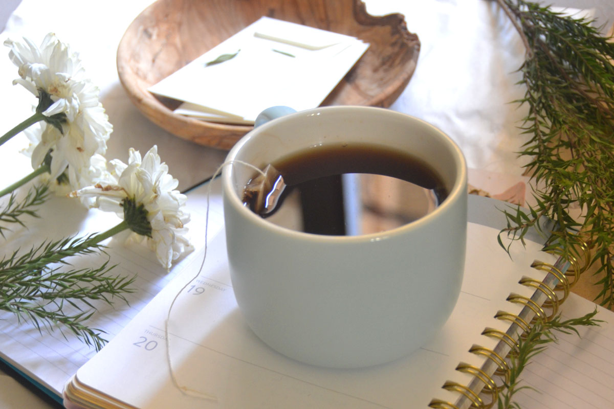 A cup of tea sits on top of a white affirmation journal.