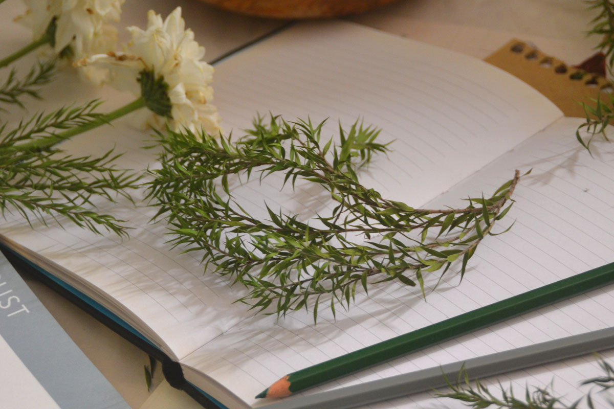 A manifestation journal lays on a table topped with flowers and greenery.