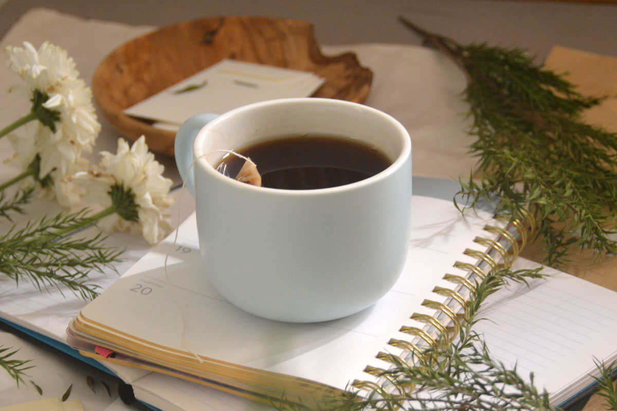A manifestation journal lays on a desk topped with a cup of tea. 