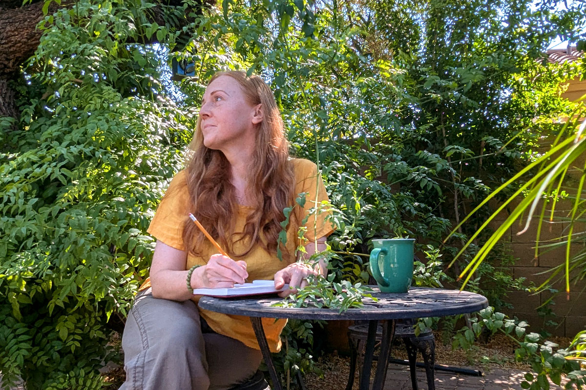 Dee sits in a garden writing in her journal.