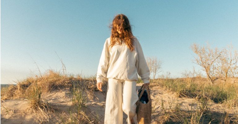 A woman in linen walks down the shore in an example of simple living.