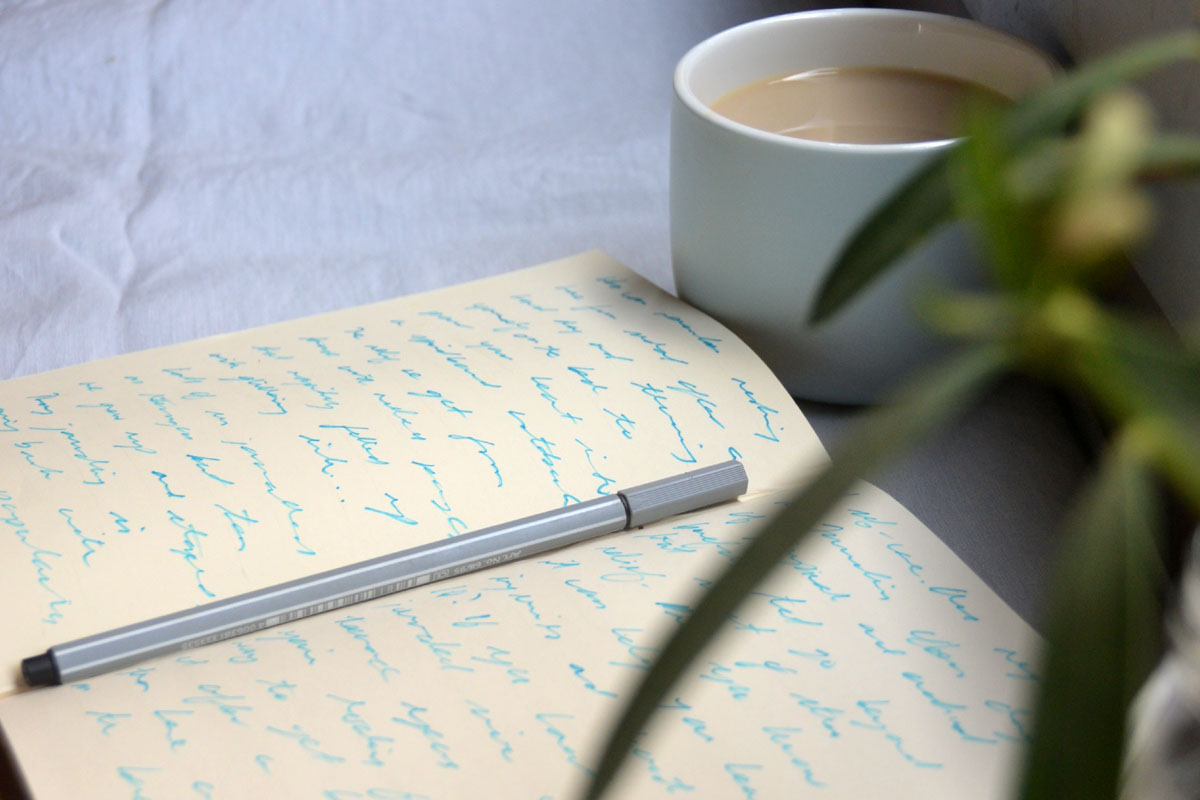 A journal lays open next to coffee and pens. 