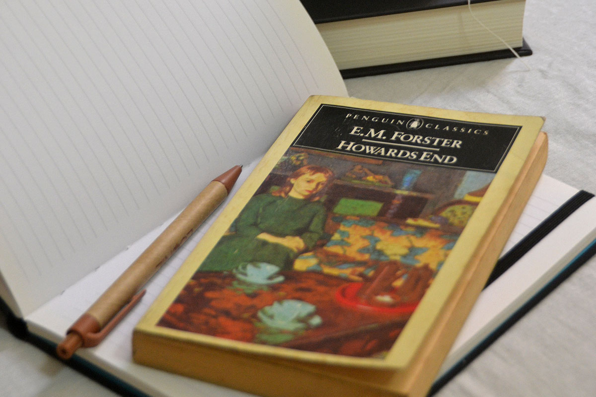 A reading journal lays on a bed next to a novel and a pen.