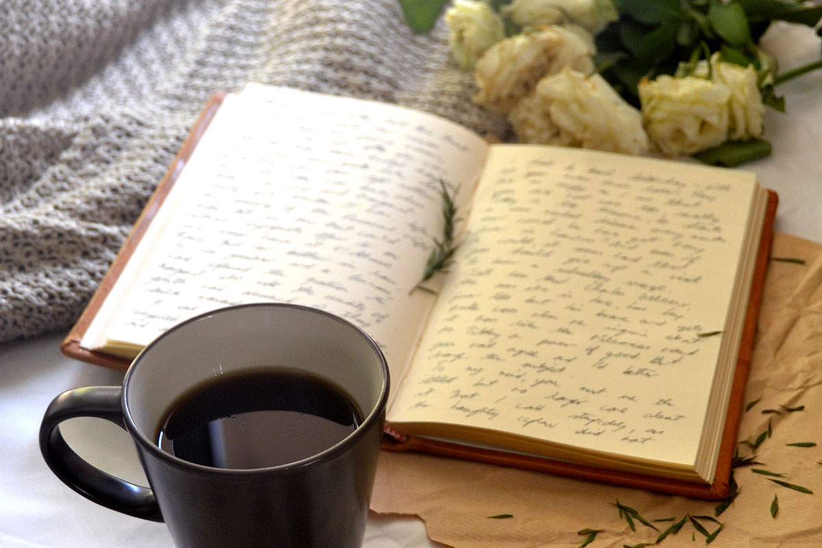 A worst case scenario journal lays on a bed next to flowers and coffee.