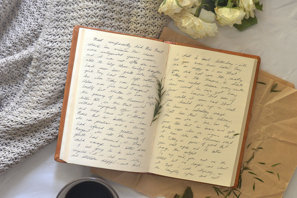 A manifestation journal lays on a bed next to flowers, filled with handwriting.