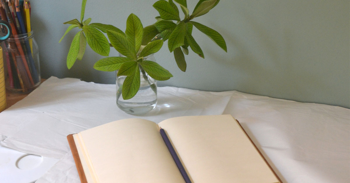 A journal lays open on a desk filled with journaling techniques next to a small vase of greenery.