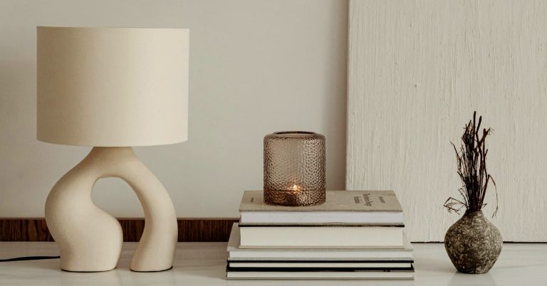 A pile of slow living books lay on a table next to a white lamp and a burning candle.