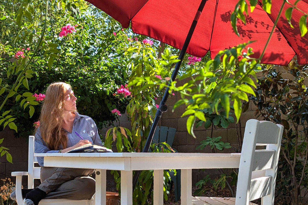 Dee sits in a garden writing in her journal.
