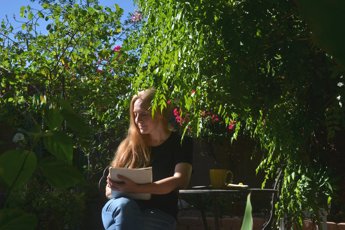 Dee sits in the garden in july with a journal of seasonal prompts. 