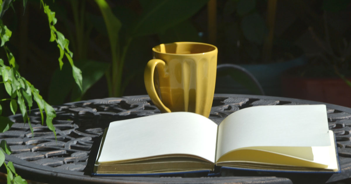 An open journal lays next to a yellow mug of tea.