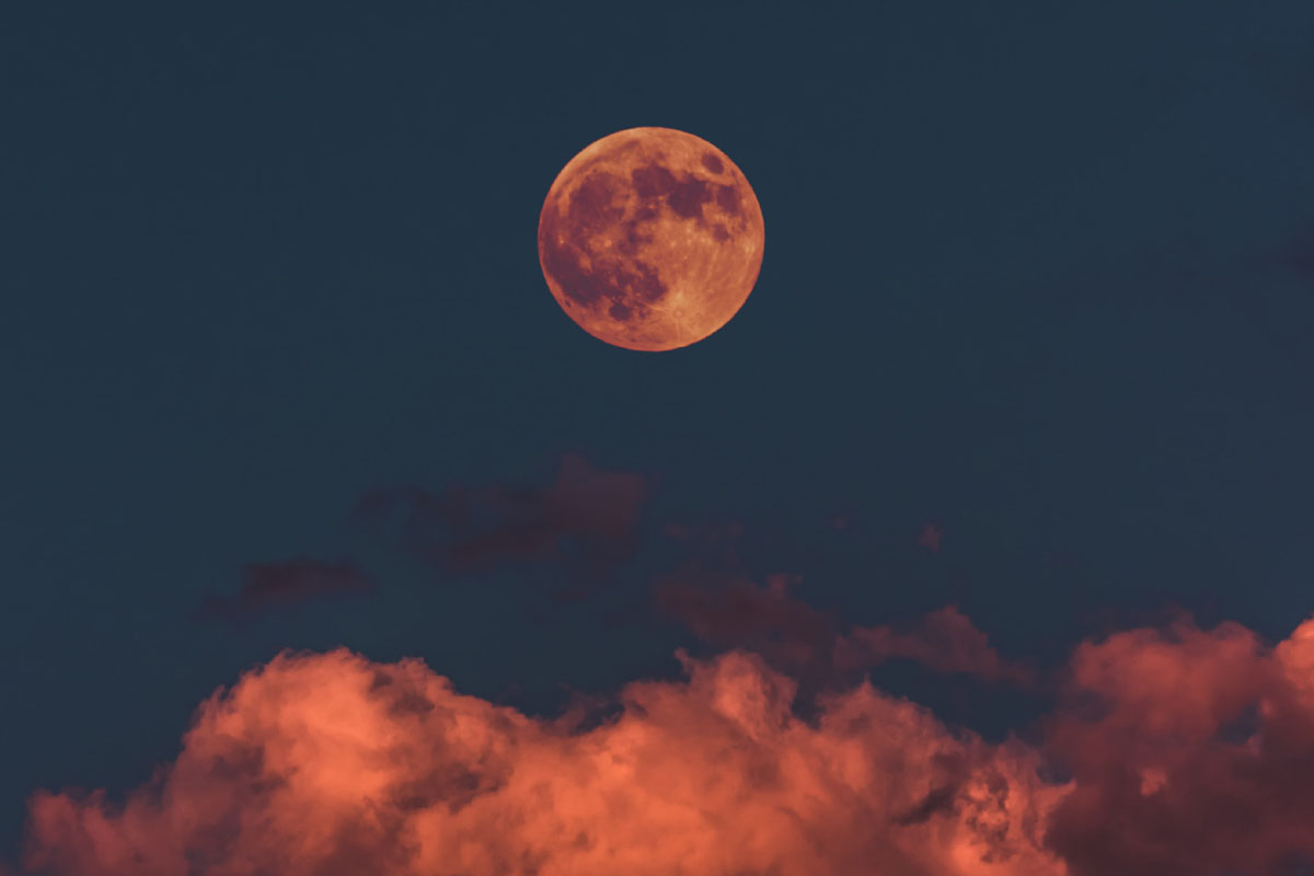 A full moon is seen in the evening above clouds. 