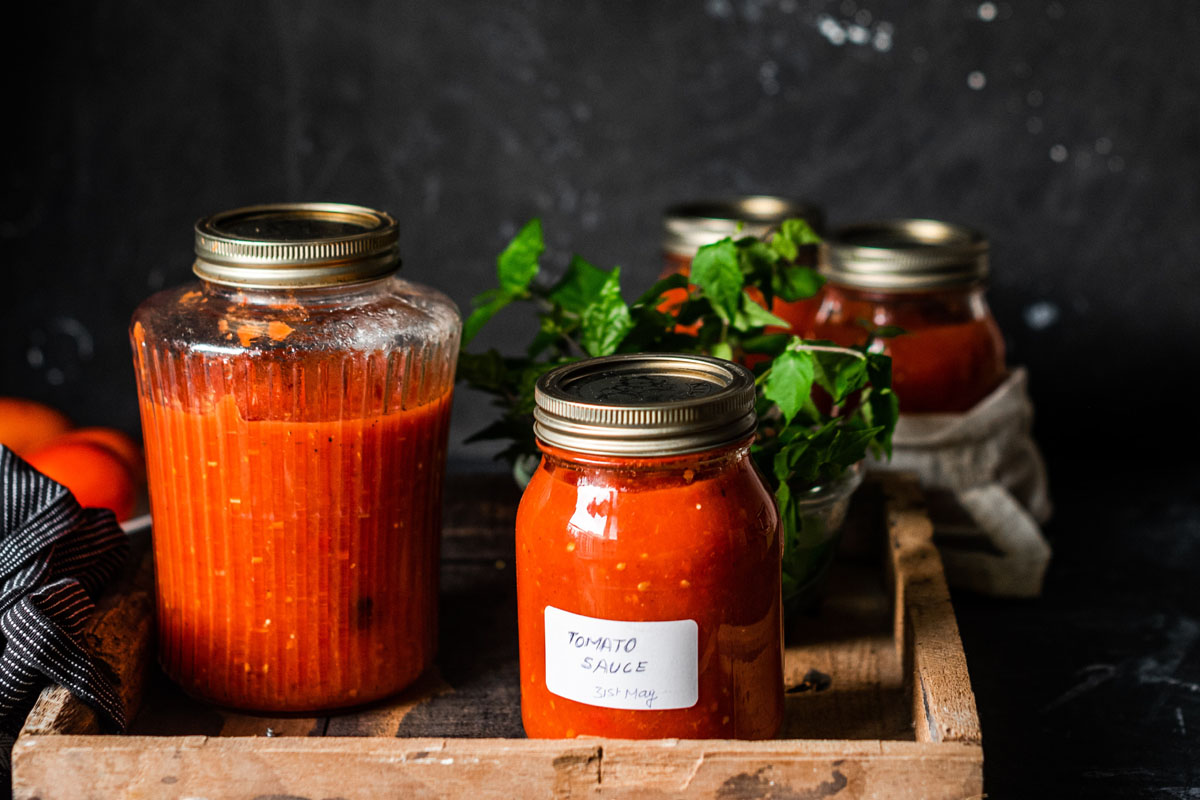 Cans of tomato paste stand on a dark table. 