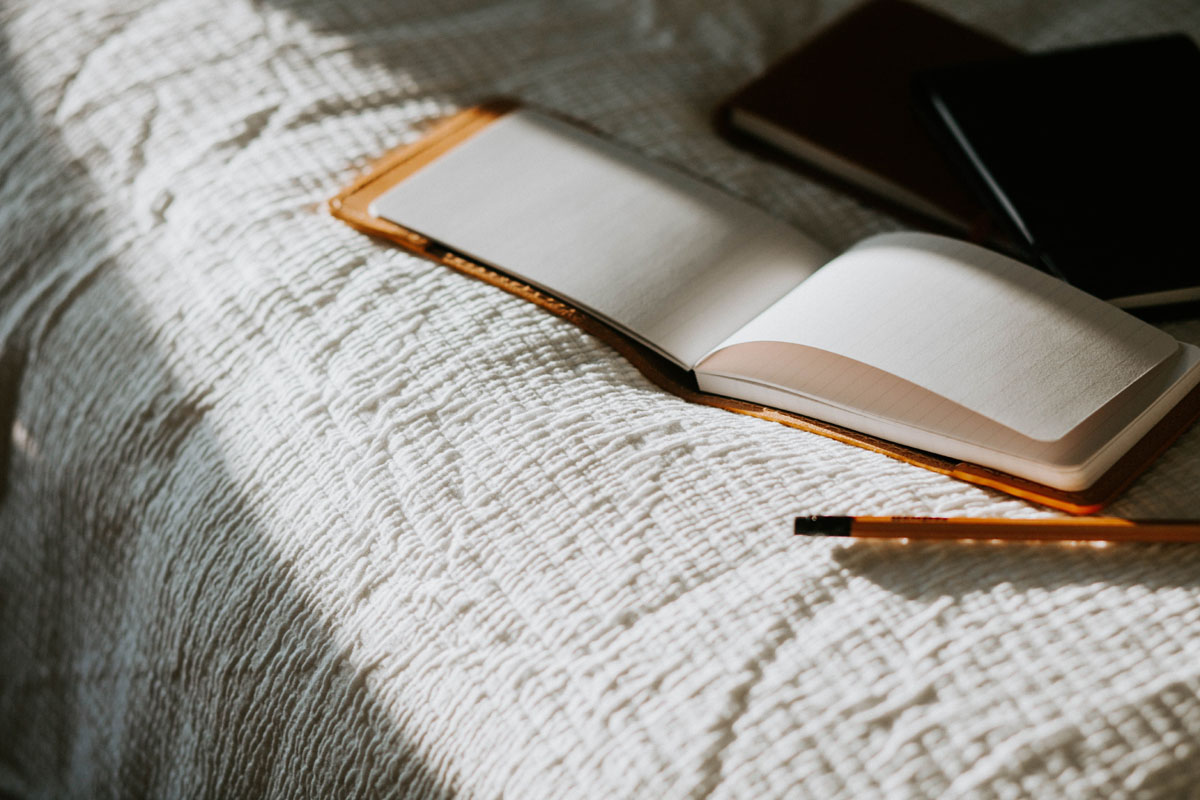 An open journal lays on a bed lit by sunlight. 