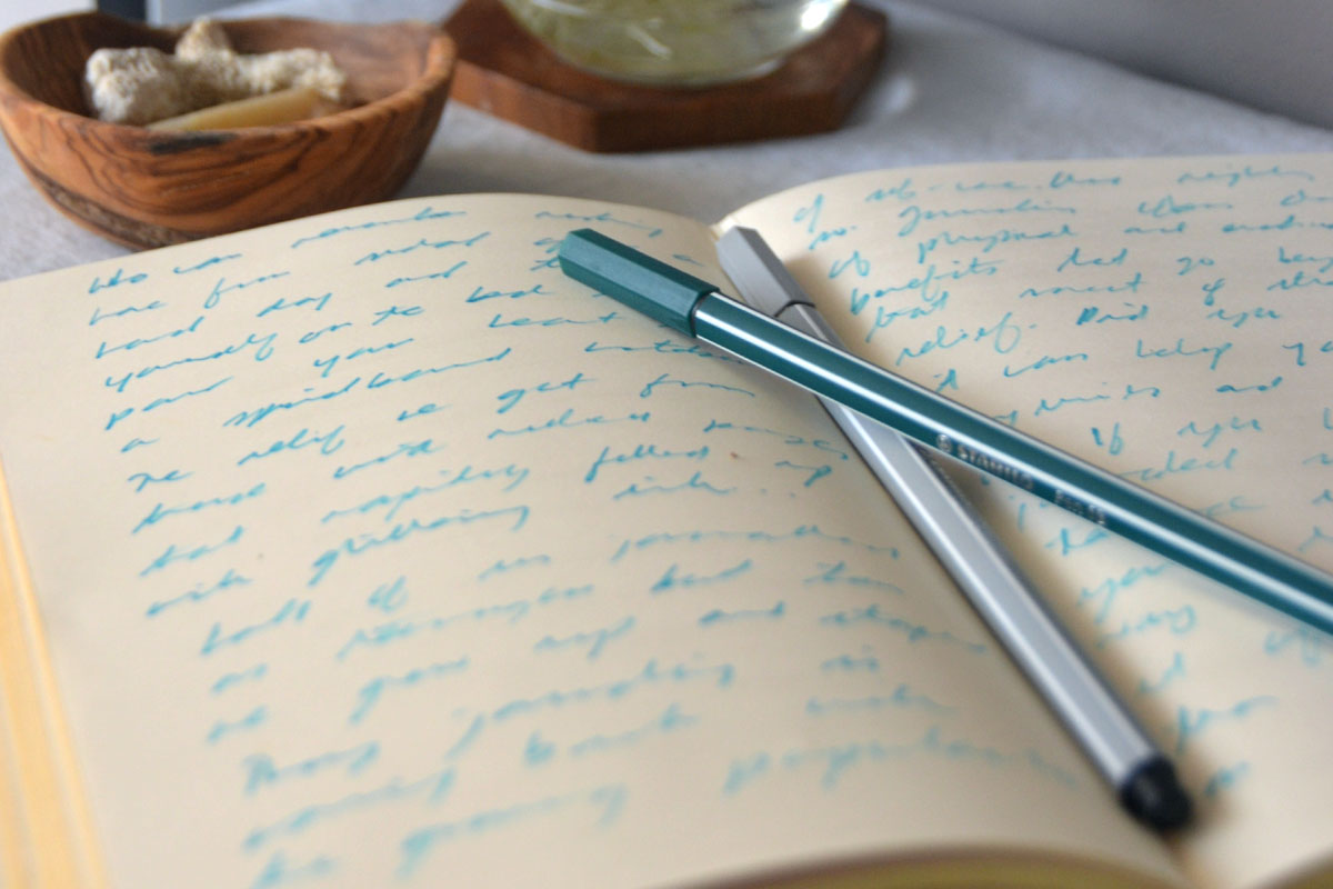 A notebook lays open with pens on top.