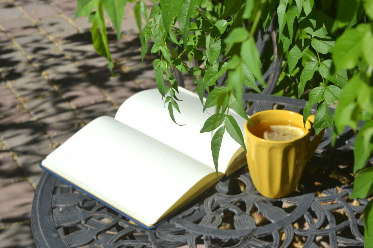 A journal lays on a table full of diary ideas alongside branches of greenery and a yellow mug.