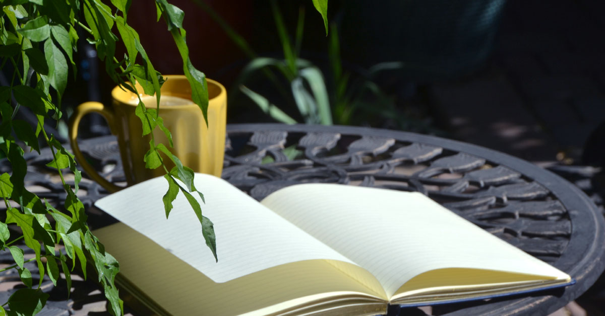 A journal lays on a table next to a tea mug full of diary ideas.