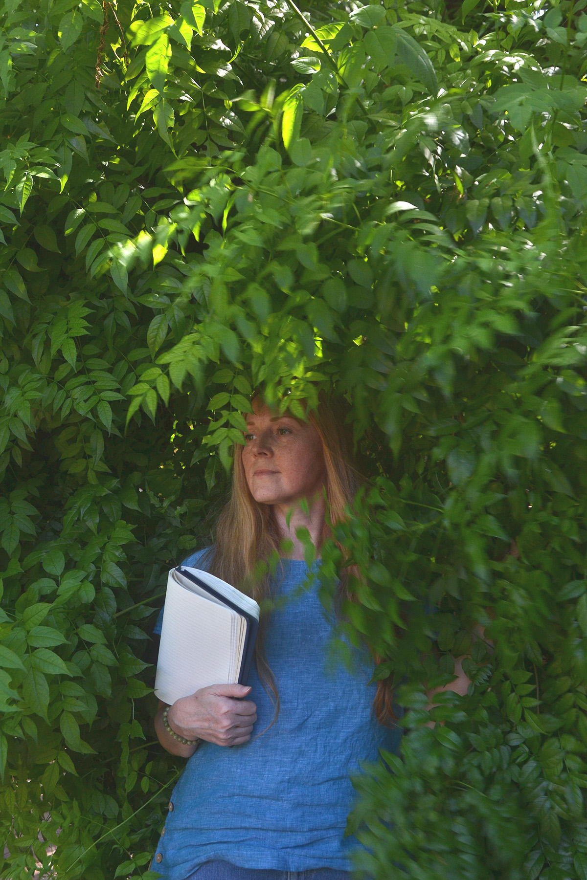 Dee stands under a tree holding her nature journal.