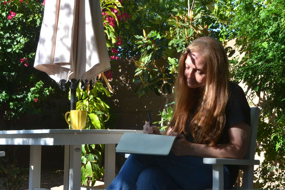 Dee sits in a garden writing in her journal.
