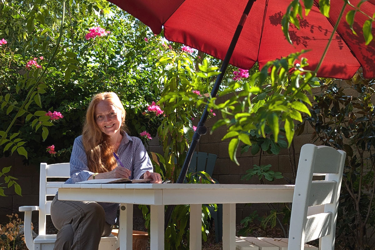 Dee sits in a garden writing in her journal.
