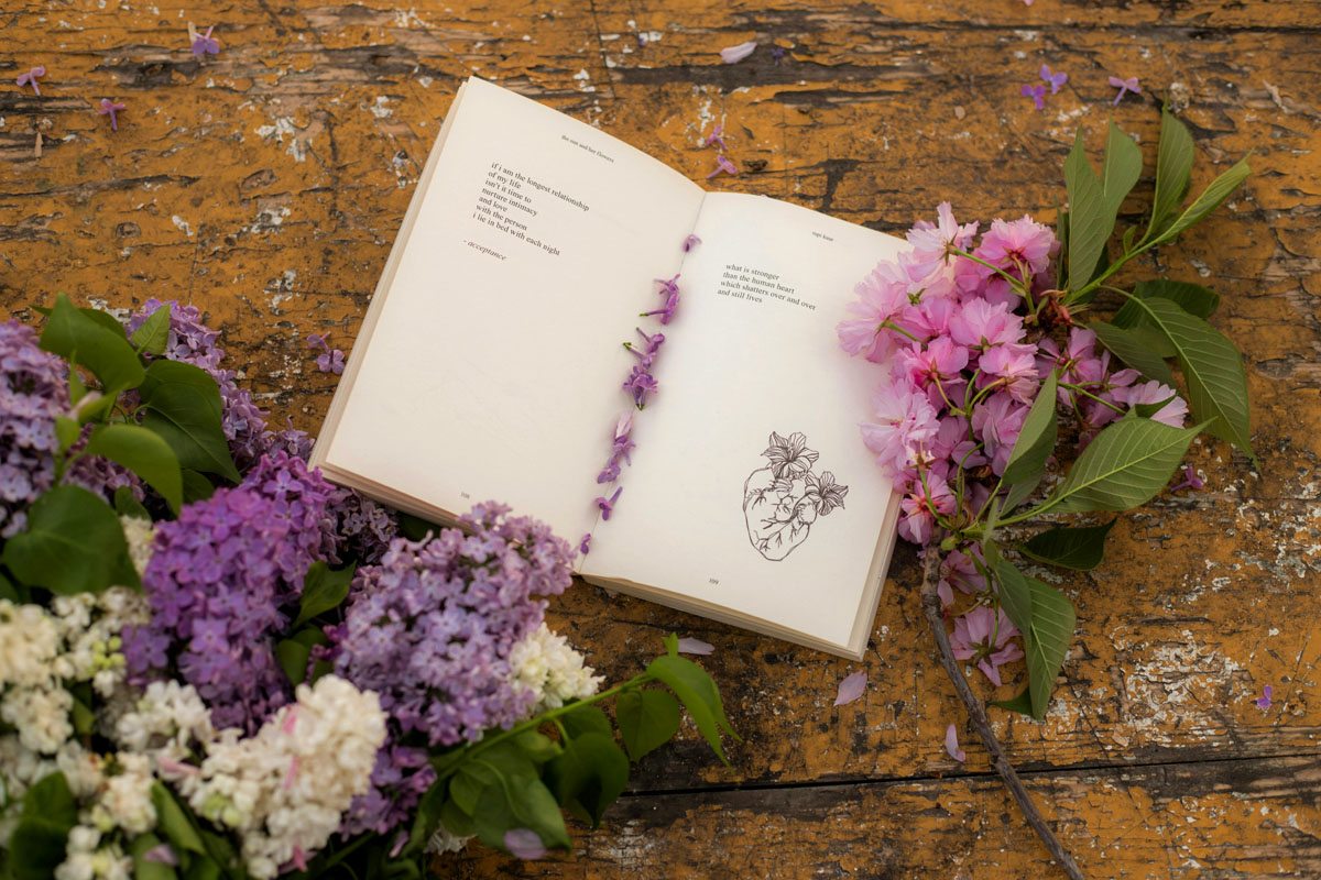 An open book lays on a wooden desk with purple flowers in the foreground during spring equinox.