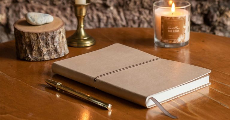 A journal full of February journaling prompts sits on a wooden table with candles in the background.