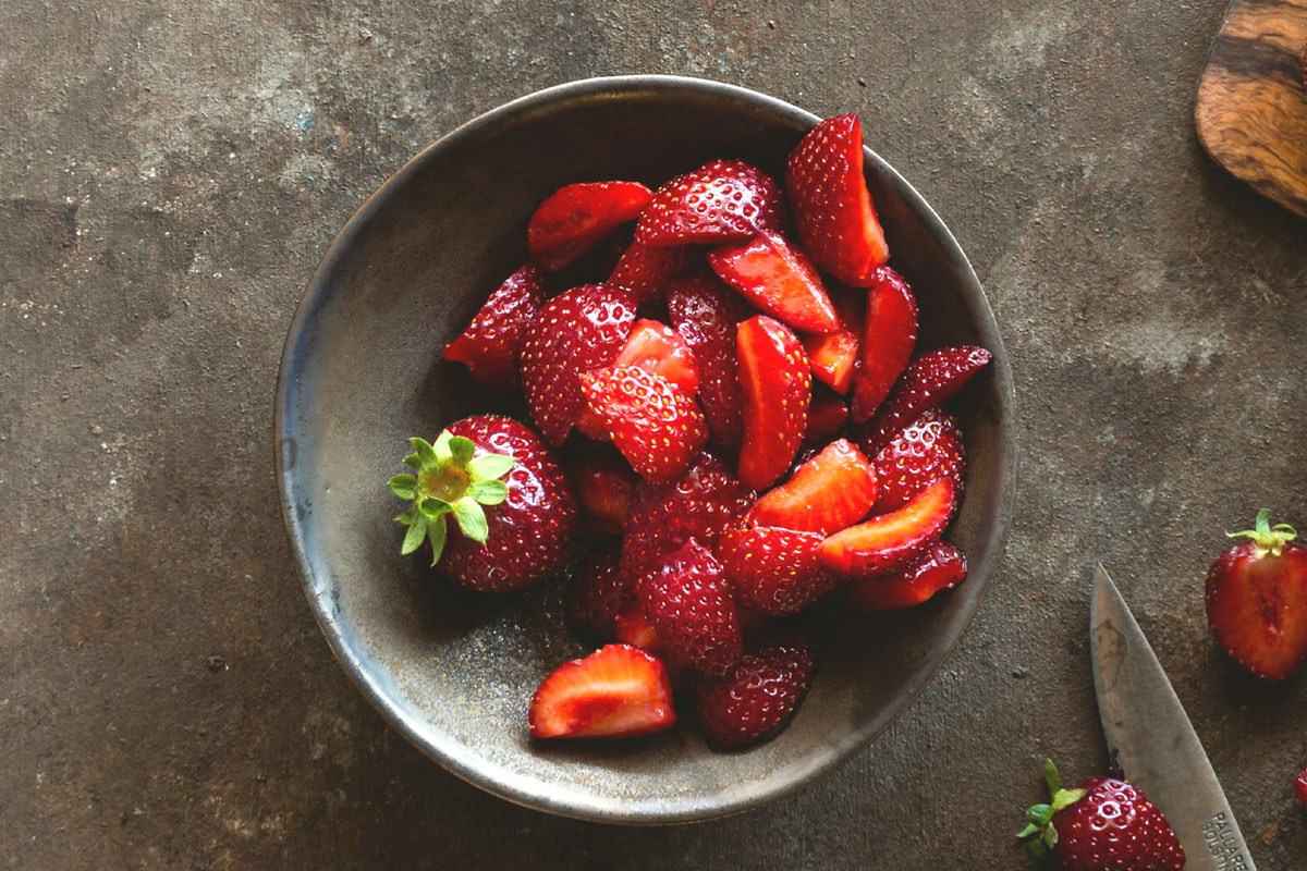 A bowl of strawberries lays on a dark table as a spring equinox salad.