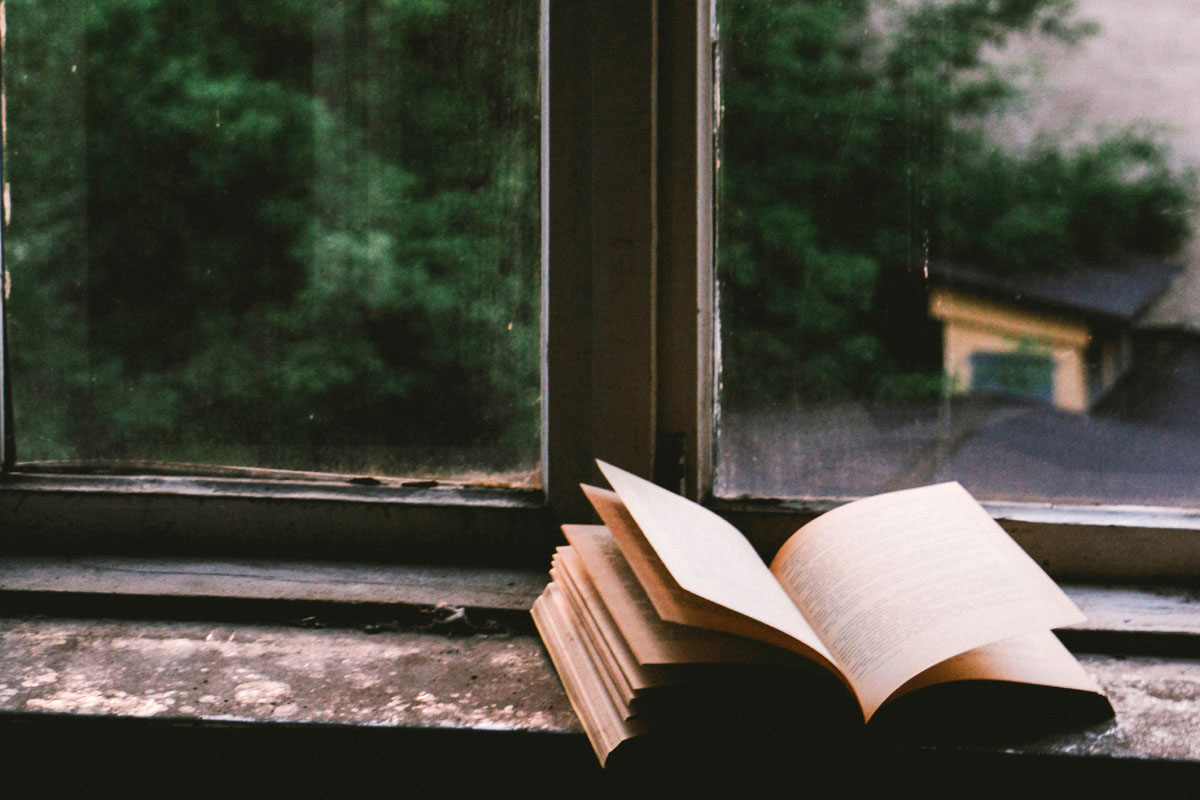 An open book lays on a windowsill.