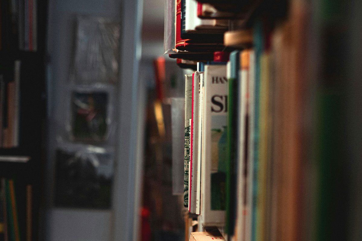 A bookshelf is shown at an angle piled with books.