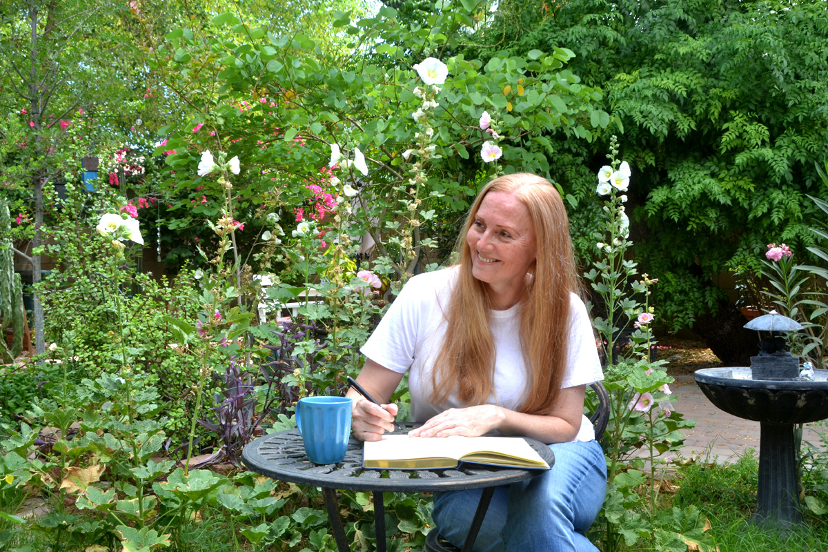 Dee sits in a garden writing in her gratitude journal.
