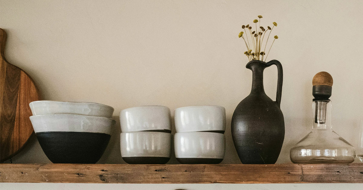 A vase, cups and plates lined up on a wooden kitchen shelf as an example of simple living.