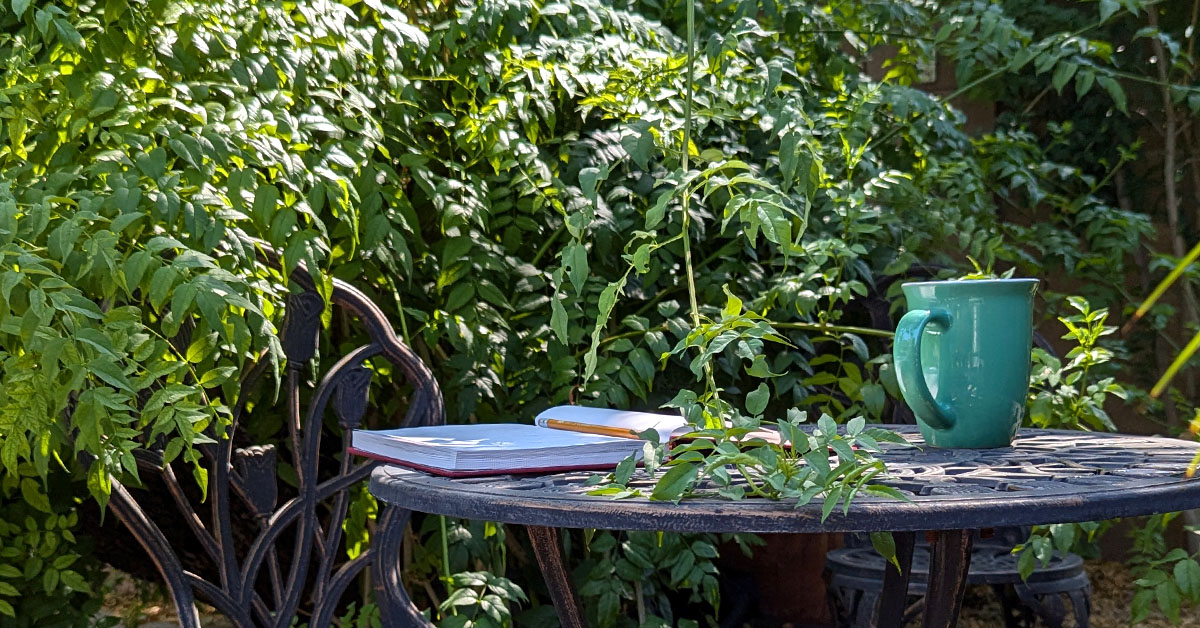 A journal lays on a patio table surrounded by greenery.