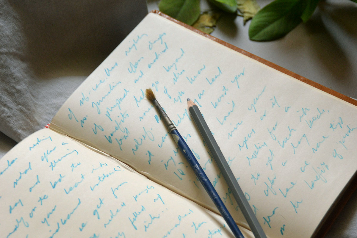 A notebook lays open with a pencil and paint brush on top.