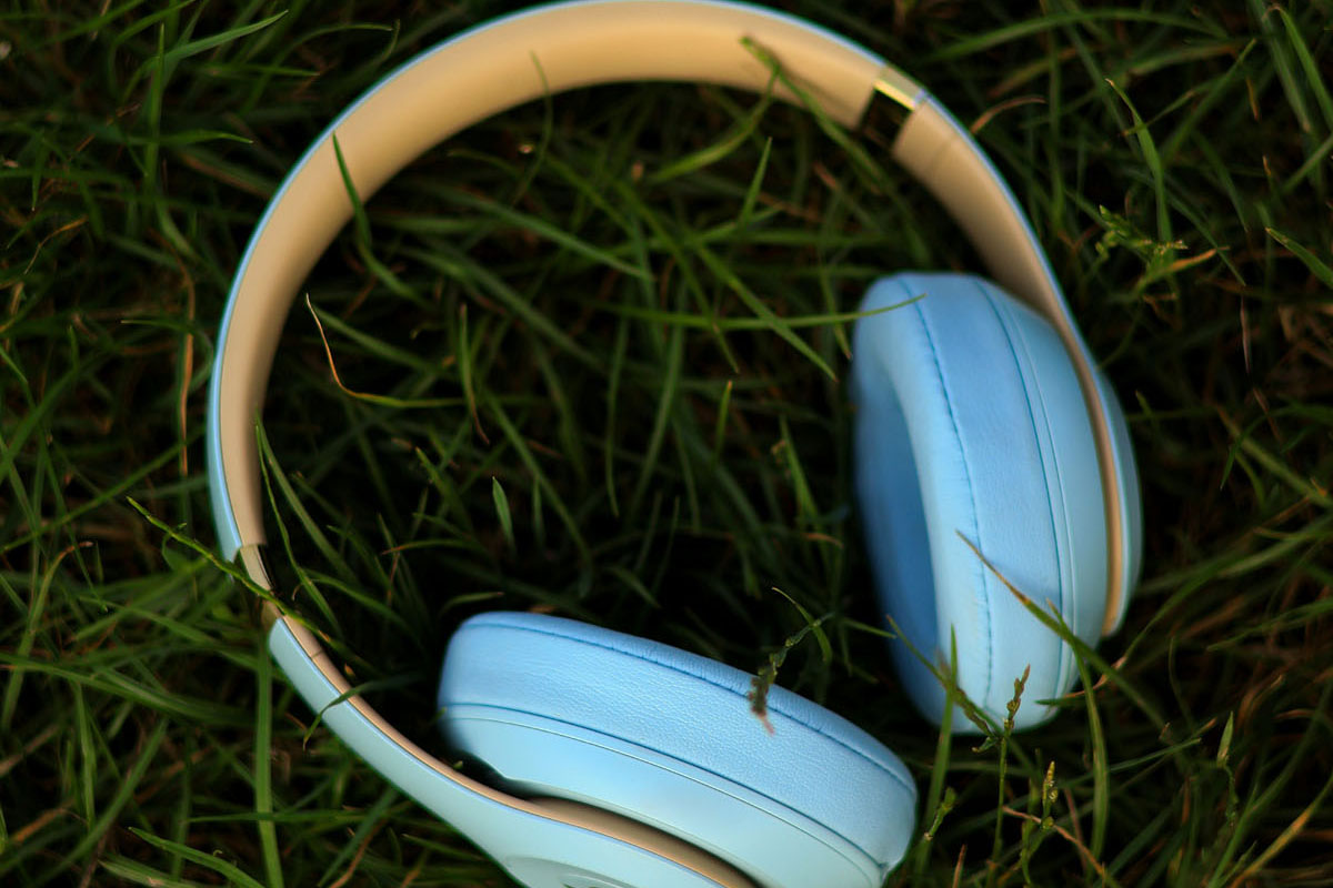 A pair of pale blue headphones lay on green grass. 