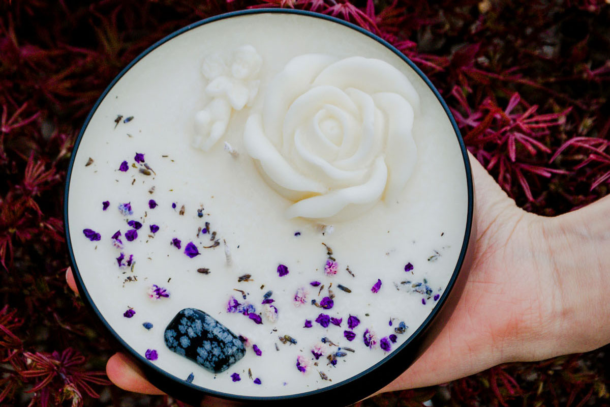 A woman holds a big white scented candle with purple petals. 